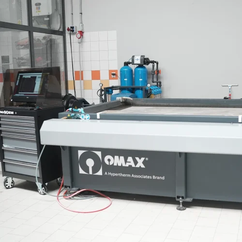 Duża, szara maszyna do cięcia strumieniem wody OMAX, marki Hypertherm Associates, z panelem sterowania i systemem filtracji wody.